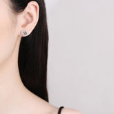 Close-up of a person wearing a heart-shaped earring with a clear gemstone on a plain background